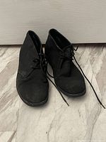 Pair of black men's lace-up boots, size 10, shown front facing with laces untied, on a textured floor.