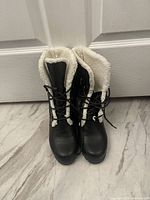 Front view of a pair of black women's winter boots showing the lace-up design and white cotton lining folded over the top edges.