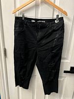 Front view of black distressed shorts hanging on hanger, showing worn fabric and distressed areas