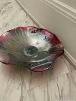 Side angle view of a multi-colored glass decorative bowl showing wavy edges and iridescent glaze.