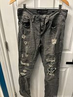 Front view of Guess ripped skinny jeans hung on hanger against white door showing ripped design and distressed detailing.