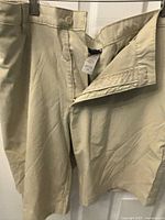 Light khaki men's shorts hanging, showing front zipper and button fly open.