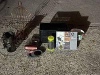 View of assorted kitchen items arranged on concrete floor, showing a metal grater, mirrored coaster, lever corkscrew box, coffee K-Cup holder, fruit stand, and decorative bowls.