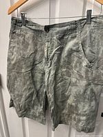 Front view of men's camo print Mossimo Supply shorts hanging on a hanger, showing button closure and pockets.