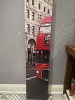 Front view of a single panel showing part of the red London double-decker bus and city background.