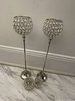 Two tall rhinestone candle holders and two smaller rhinestone candle holders placed on the floor against a wall, showing their full height and design.