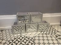 Front view of set of 5 mirrored decorative boxes arranged in pyramid shape on patterned tile floor, showing mirror panels and mosaic borders.