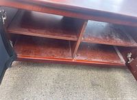 Close-up of lower section of TV stand with open cabinet doors showing shelf inside and worn surfaces.