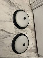Two round LED ceiling lights placed on a tiled floor, showing the front frosted domes and black trim with a central knob.