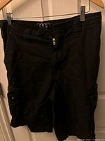 Front view of black CSG men's shorts showing buttoned flap side pockets and zip fly