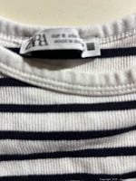 Close-up photo of the neckline showing the Zara brand label and size small tag, with horizontal black and white stripes visible.