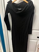 Front view of the black long dress showing off-shoulder neckline and long sleeves hanging on wooden hanger.