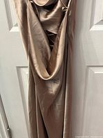 Front view of the beige/light champagne silk gown with cowl neck and spaghetti straps hung on a door showing the draped fabric and sheen.