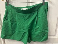 Front view of bright green Zara shorts hanging on a hanger, showing waistband and front detailing.