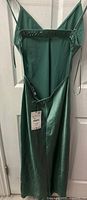 Full view of the green silk gown hanging on a door, showing spaghetti straps, attached Zara tag, and length with slit.