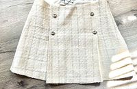 Front view of Zara mini skirt showing the textured beige tweed fabric and decorative buttons.
