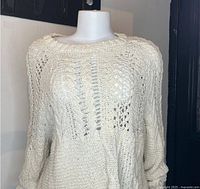 Front view of cream-colored knitted sweater on mannequin showing cable and open knit patterns.