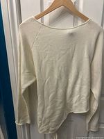Front view of a cream Zara long sleeve top on a wooden hanger showing the fabric and style.