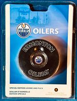 Front view of the special edition set showing the black puck with the $1 coin embedded in the center and packaging showing Oilers logo and Royal Canadian Mint logo.