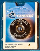 Front view of sealed collectible showing puck with embedded coin and Vancouver Canucks branding in original packaging.