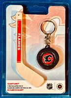 Front view of sealed package showing wooden mini stick and mini puck keychain with Calgary Flames logos.