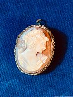 Front view of the oval hand carved cameo brooch featuring a woman's profile in shell set within a detailed sterling silver frame.