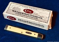 Top view of the Case Doctor's Cutter 3185 CV folding knife with ivory colored handle scale and metal bolster ends, next to its original white cardboard branded box with red and black print.