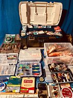 Wide shot showing large black tackle box, clear organizers, wood fly box, metal fly tin, spools of line and lure compartments