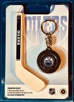 Photo showing the full sealed blister pack containing the mini hockey stick and mini puck keychain with Edmonton Oilers logo and text.