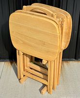 Four solid wood folding occasional tables with rounded rectangular tops and handles, set on and off the folding stand designed for compact storage.