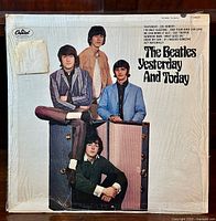 Front cover of The Beatles Yesterday and Today album showing four band members seated and standing around suitcases, sealed in shrink wrap with some visible wear.