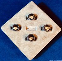 Four vintage Beatles metal gumball rings on a cream fabric display pad, showing all four individual ring faces each with a Beatles member's image.