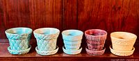 All five McCoy pottery planters and saucers arranged in a row, showing varying colors and raised patterns.