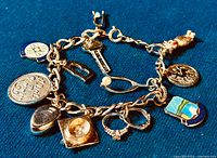 Close-up showing full chunky sterling silver charm bracelet with multiple distinct charms including atom symbol, key, safety pin, coin, shell, and enamel charms.