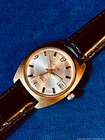 Close-up of silver dial showing Clifton branding, date window at 3 and applied gold markers