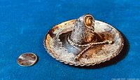 Top angled view of the sterling silver sombrero shaped ashtray with detailed floral engravings and a dime for size reference.