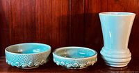 Full front view of the three McCoy pottery pieces; two low round dishes/planters with decorative raised patterns and a tall flared vase.