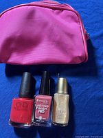 Three nail polish bottles (CND, Rimmel, Yria) next to a pink cosmetic bag on blue background.