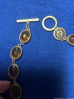 Close-up of toggle clasp showing decorative circular emblem and three oval yellow stones.
