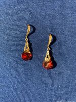 Pair of gold tone dangle earrings with large round red faceted gemstones and small clear stones in the curved top setting.