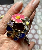 Close-up photo of ring showing detailed enamel flowers and butterfly design on gold-tone metal.