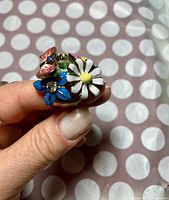 Close up front view of enamel floral ring showing three flowers in white, pink, and blue.