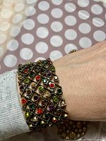 Photo showing bracelet worn on wrist with multicolor gemstones and gold-tone lattice design visible