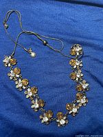 Full view of necklace on blue background showing the amber and clear faceted round gemstones in prong settings along metal chain.