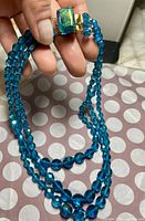 Photo of blue faceted beaded necklace held in hand showing two strands and gemstone clasp.