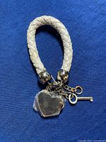 White braided leather bracelet or bag fastener with metallic heart-shaped lock and small key.