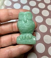 Front view of the small green stone owl figurine held in a hand, showing detailed carving on the face and feathers.