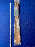 Shoe horn still in sealed plastic packaging laid next to a 14-inch tape measure on blue fabric background.