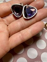 Close-up view of one earring held in hand showing triangular violet faceted gemstone in silver-tone bezel setting.