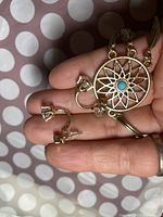 Close-up photo of the gold-tone clip-on earrings with clear gemstone and the dreamcatcher keychain with turquoise stone and feather charm being held in hand.